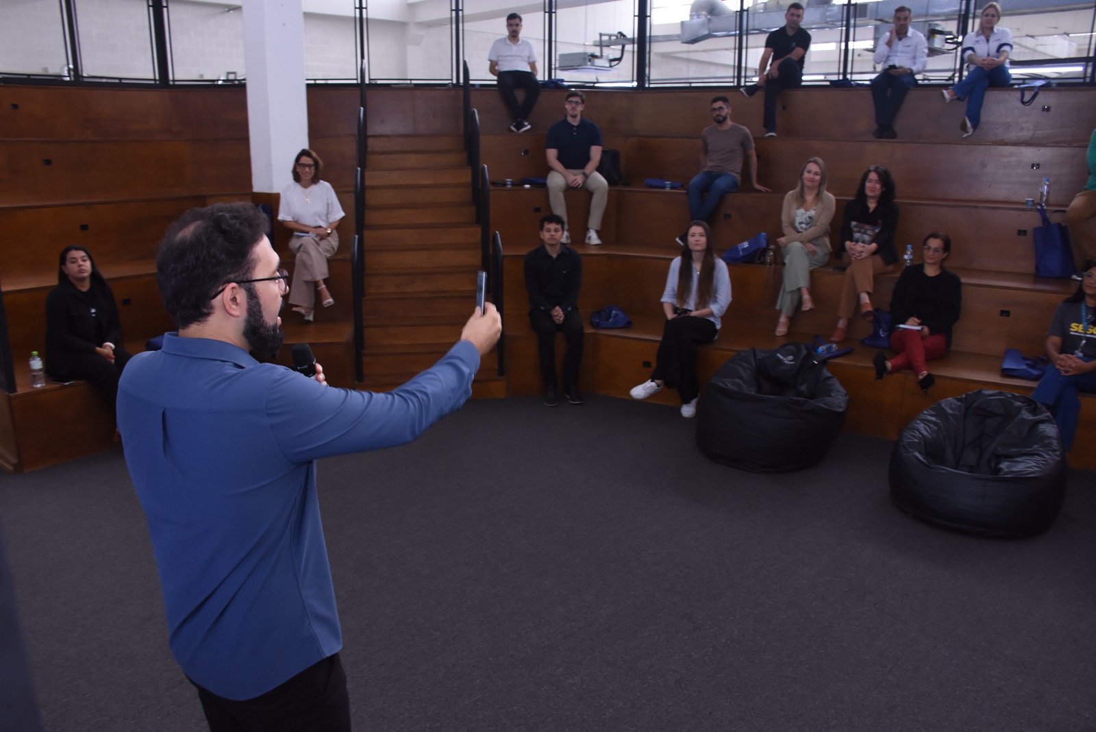 Calebe Salvia, de costas, conduz uma palestra para empresários sentados em uma arquibancada de madeira