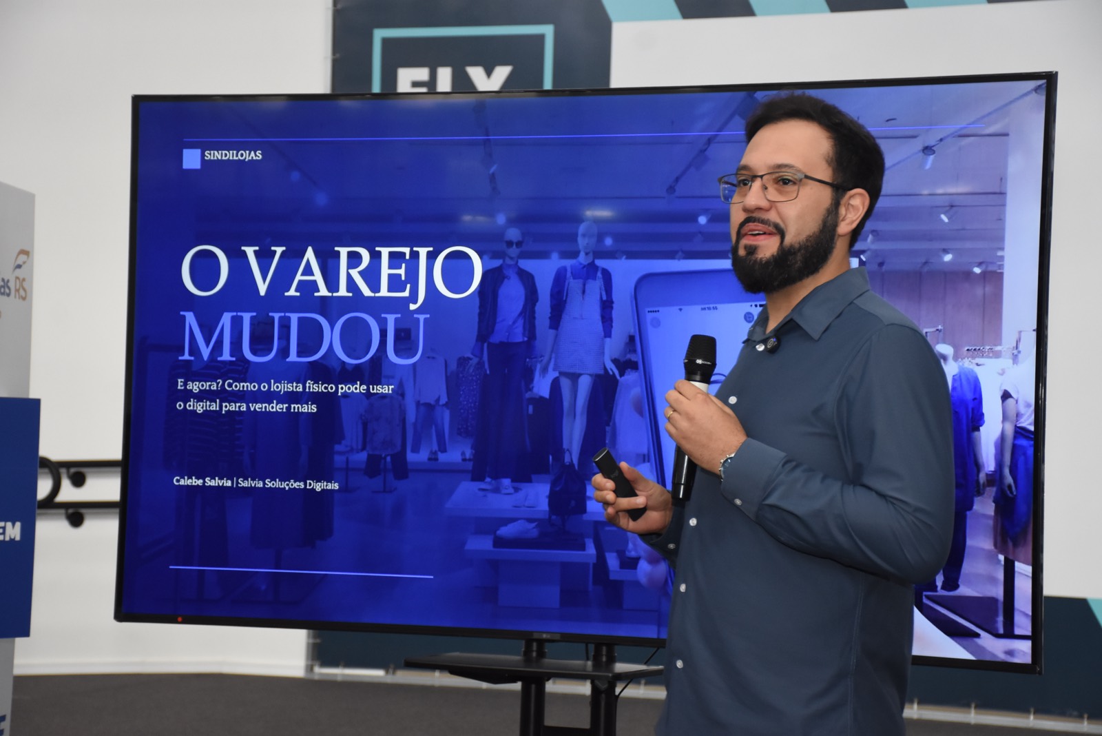 Calebe Salvia apresenta, diante de um telão, a palestra O varejo mudou, sobre como o lojista físico pode usar o digital para vender mais