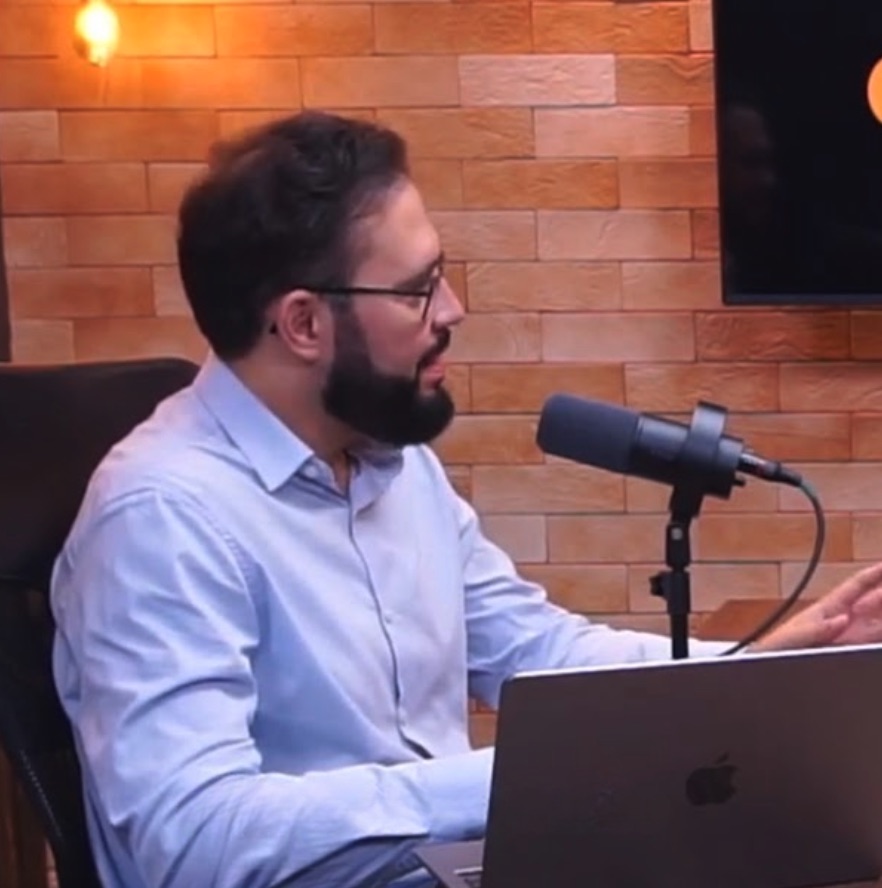 Calebe Salvia gravando um podcast, sentado diante de um microfone e de um notebook